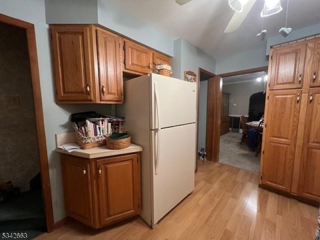 kitchen featuring brown cabinetry, ceiling fan, freestanding refrigerator, light countertops, and light wood-type flooring