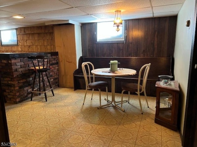 dining space featuring a wealth of natural light, a drop ceiling, wood walls, and a dry bar