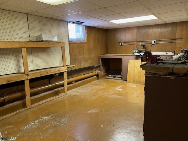 basement featuring wood walls, a workshop area, and a drop ceiling