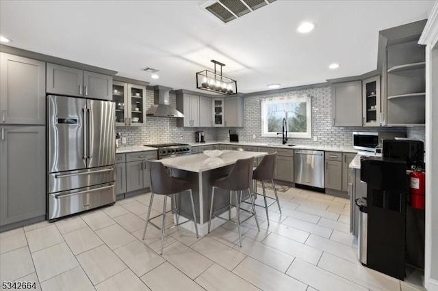 kitchen featuring gray cabinets, visible vents, appliances with stainless steel finishes, a sink, and wall chimney range hood