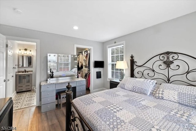 bedroom with baseboards, a closet, a walk in closet, light wood finished floors, and ensuite bath