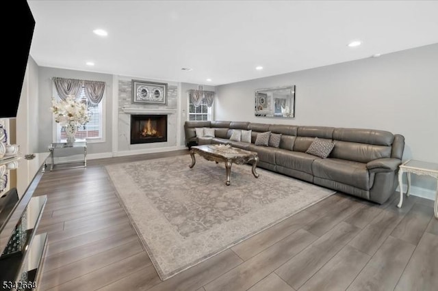 living area featuring baseboards, a lit fireplace, wood finished floors, and recessed lighting