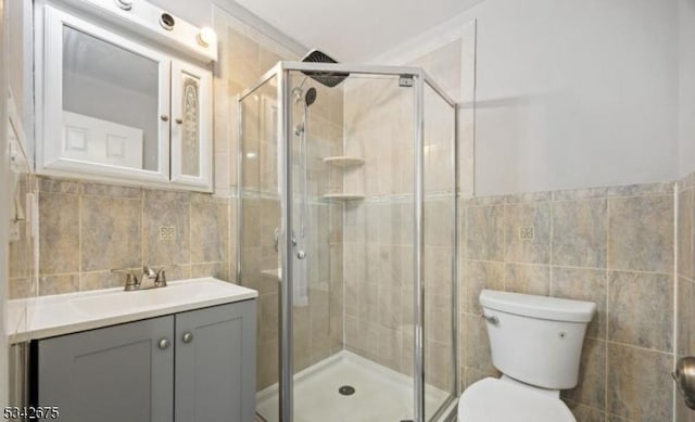 bathroom with toilet, a stall shower, tile walls, and vanity