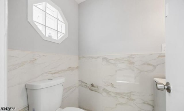 half bath with tile walls, toilet, and a wainscoted wall