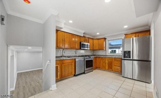 kitchen with brown cabinets, a sink, tasteful backsplash, appliances with stainless steel finishes, and light stone countertops