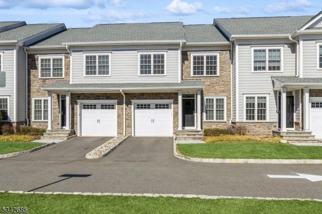 view of property featuring stone siding, driveway, an attached garage, and a shingled roof