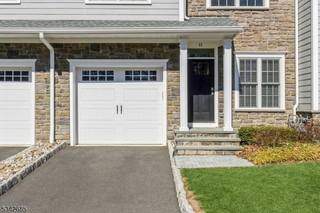 entrance to property with aphalt driveway, a garage, and a shingled roof