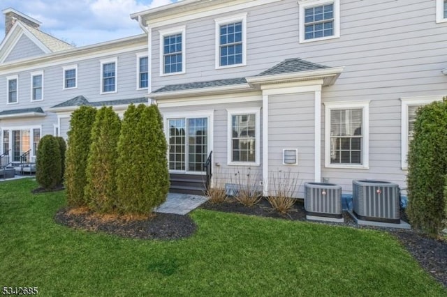 back of house featuring central AC unit, entry steps, and a lawn