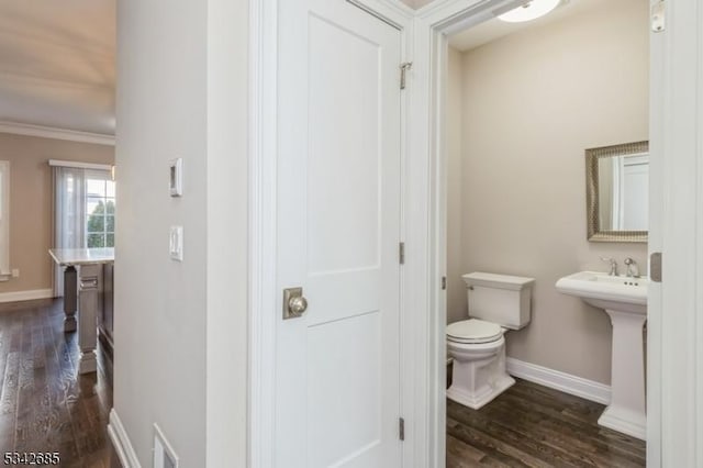 half bathroom featuring toilet, crown molding, baseboards, and wood finished floors