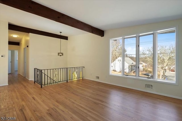 unfurnished room featuring beam ceiling, baseboards, and wood finished floors