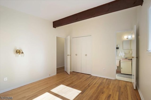 unfurnished bedroom with beam ceiling, ensuite bath, wood finished floors, a closet, and baseboards