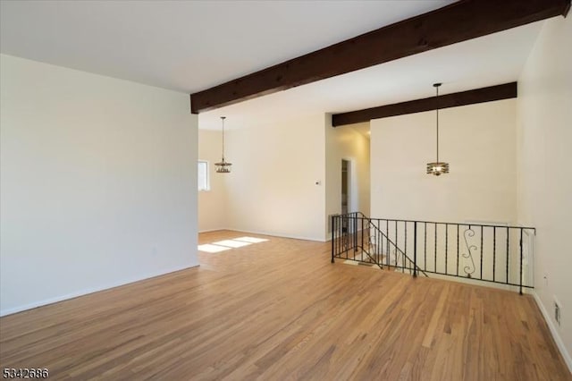 spare room featuring lofted ceiling with beams, wood finished floors, and baseboards