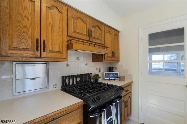 kitchen with decorative backsplash, light countertops, black range with gas cooktop, and brown cabinets