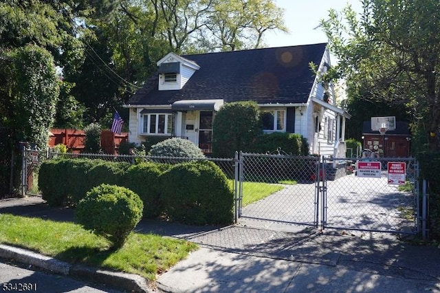 new england style home with a shingled roof, a fenced front yard, and a gate