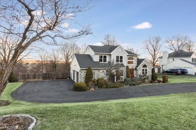 view of front of property featuring stone siding, a front lawn, fence, and driveway