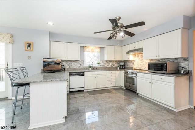 kitchen with appliances with stainless steel finishes, white cabinets, a sink, a peninsula, and under cabinet range hood