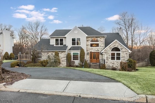 view of front of home featuring aphalt driveway, a shingled roof, fence, a chimney, and a front yard