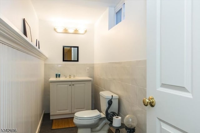 half bath featuring wainscoting, toilet, wood finished floors, vanity, and tile walls