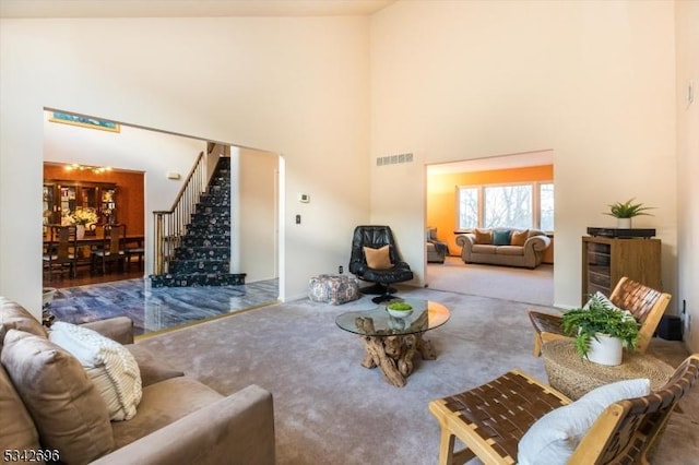 living room featuring stairway, carpet, a towering ceiling, and visible vents