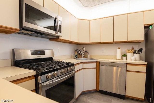 kitchen featuring light wood finished floors, light countertops, appliances with stainless steel finishes, cream cabinets, and a sink