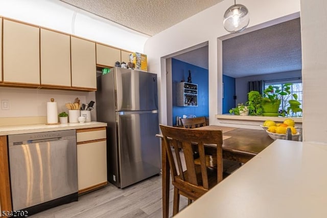 kitchen featuring light countertops, stainless steel appliances, light wood-style floors, cream cabinetry, and a textured ceiling