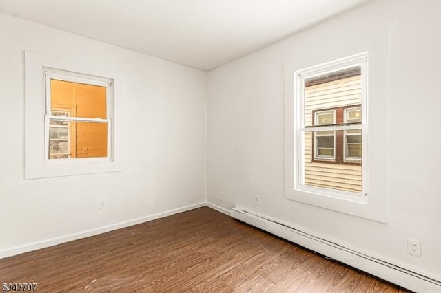 unfurnished room with a baseboard heating unit, baseboards, dark wood-type flooring, and plenty of natural light