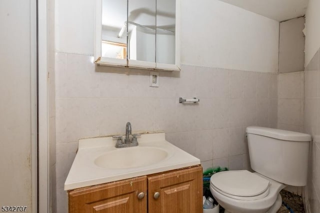 half bathroom featuring toilet, tile walls, and vanity