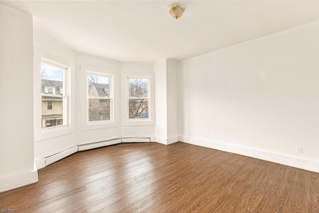 empty room featuring a baseboard heating unit, baseboards, and wood finished floors