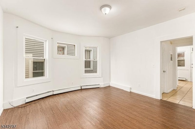 unfurnished room with a baseboard heating unit, baseboards, and wood finished floors