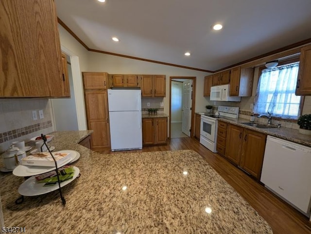 kitchen with white appliances, lofted ceiling, light stone counters, crown molding, and a sink