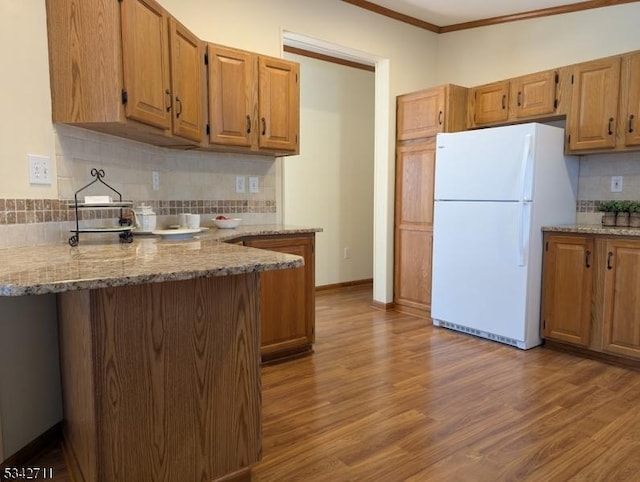 kitchen featuring wood finished floors, backsplash, freestanding refrigerator, light stone countertops, and baseboards