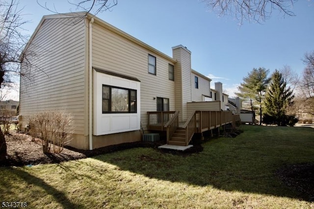 back of property with a deck, a lawn, and a chimney