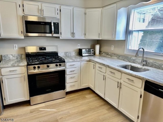 kitchen with a sink, light stone countertops, appliances with stainless steel finishes, and light wood finished floors