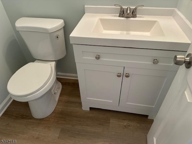 half bath featuring baseboards, toilet, wood finished floors, and vanity