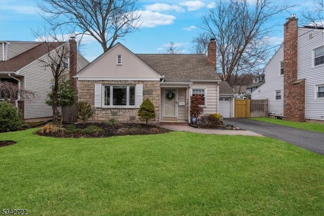 view of front facade featuring driveway, stone siding, roof with shingles, a front lawn, and a chimney