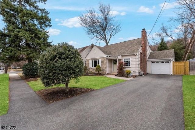 view of front of house with fence, a garage, stone siding, driveway, and a front lawn