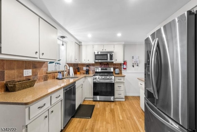 kitchen with appliances with stainless steel finishes, a sink, white cabinets, and tasteful backsplash