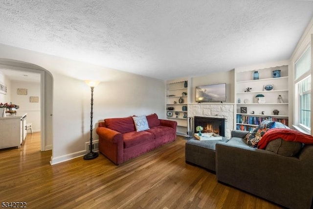 living area featuring arched walkways, a warm lit fireplace, a textured ceiling, and wood finished floors