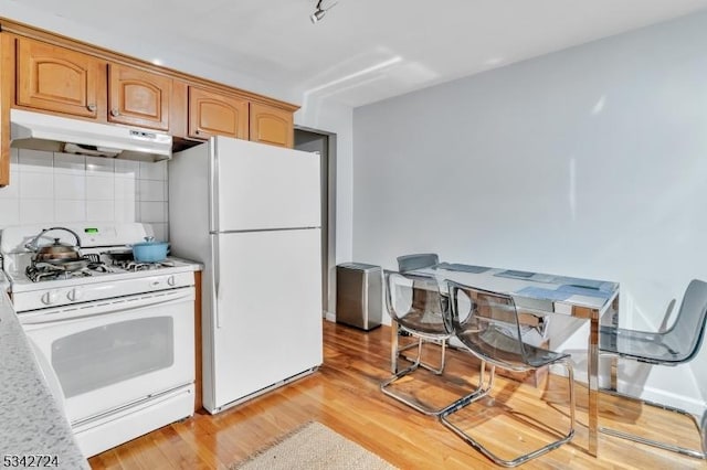 kitchen featuring under cabinet range hood, white appliances, light wood-style floors, light countertops, and tasteful backsplash