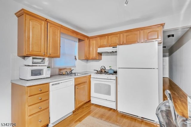 kitchen featuring light wood-style flooring, under cabinet range hood, white appliances, a sink, and light countertops