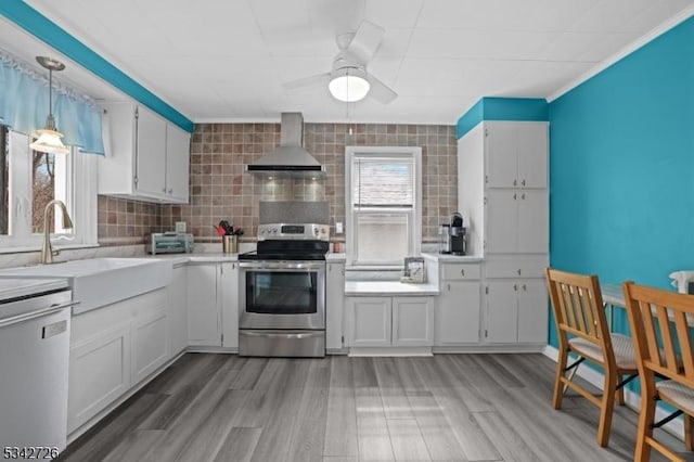 kitchen featuring light countertops, appliances with stainless steel finishes, white cabinets, a sink, and wall chimney range hood