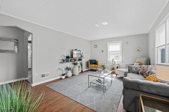 living room with arched walkways, wood finished floors, visible vents, baseboards, and crown molding