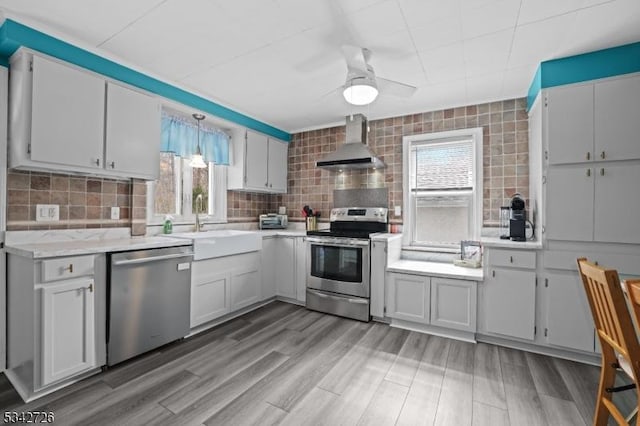 kitchen featuring stainless steel appliances, light countertops, backsplash, a sink, and wall chimney exhaust hood