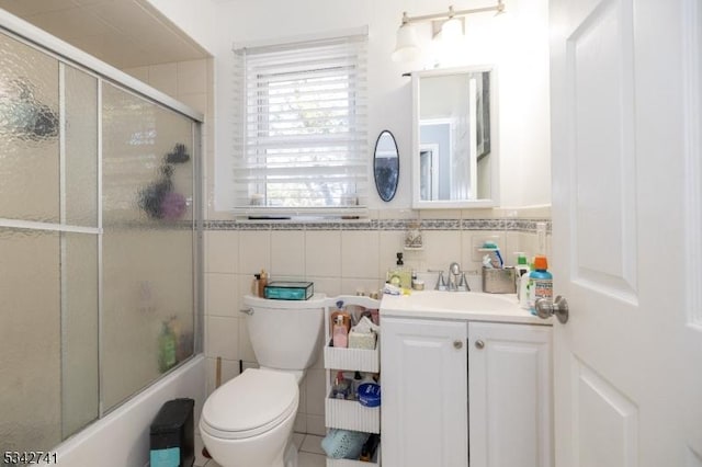 bathroom featuring toilet, bath / shower combo with glass door, tile walls, and vanity