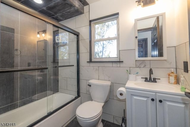 bathroom featuring toilet, shower / bath combination with glass door, tile walls, and vanity