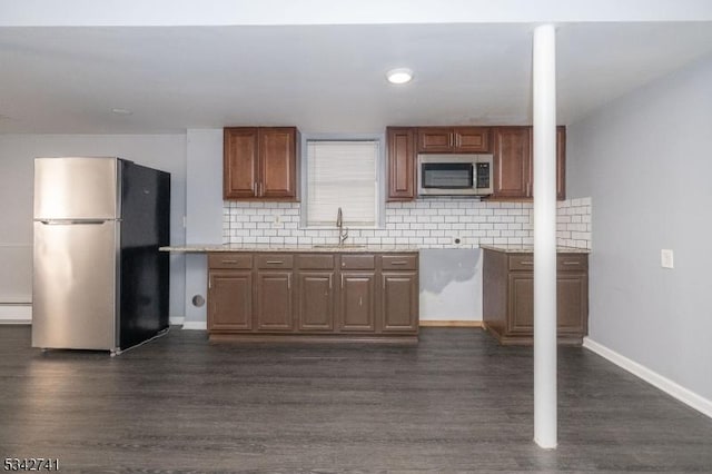 kitchen with appliances with stainless steel finishes, dark wood finished floors, a sink, and backsplash