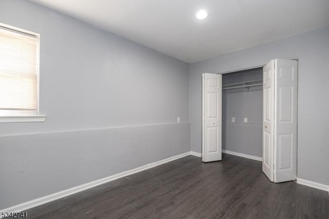 unfurnished bedroom featuring dark wood-style flooring, a closet, and baseboards