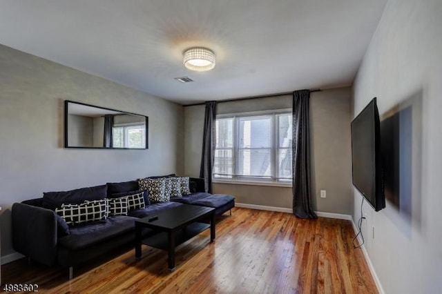 living area with visible vents, plenty of natural light, baseboards, and wood finished floors