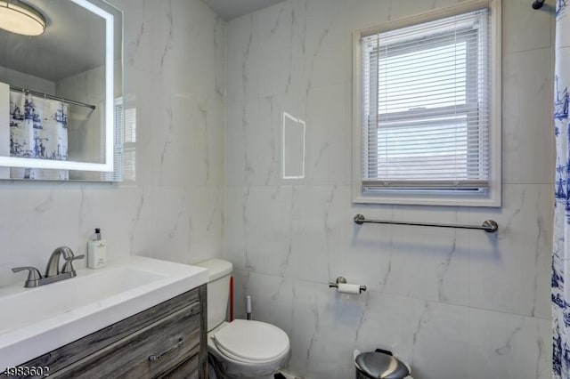 full bath with a shower with shower curtain, toilet, vanity, and tile walls