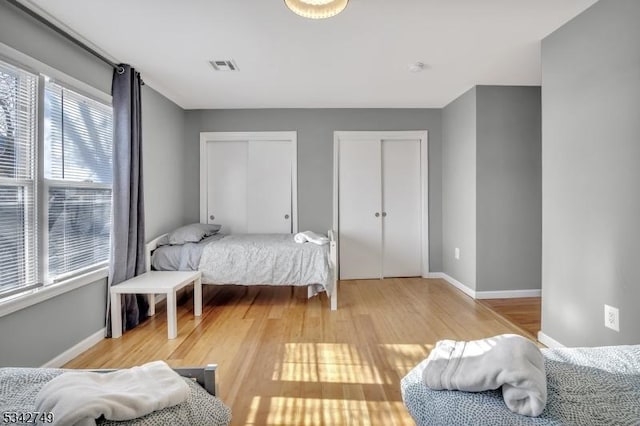 bedroom with light wood-type flooring, baseboards, visible vents, and multiple closets